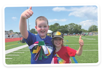 Two Children at track and field giving thumbs up with ribbons pinned to chest