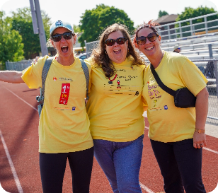 three spectators posing together on the track smiling wearing sunglasses and yellow shirts in support of the special olympics