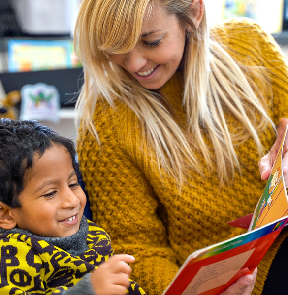 A teacher reading a picture book with a young student in a classroom