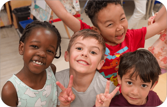 Four children posing together in a classroom, with two children holding up peace signs.