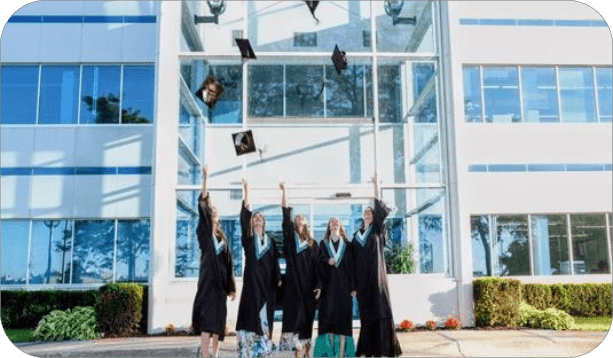 Group of graduates celebrating outside a school building by tossing their graduation caps.