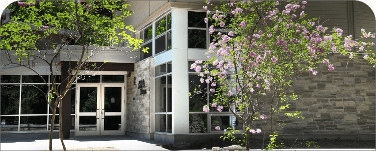 Exterior entrance of the Living Campus building, surrounded by trees and flowering plants.