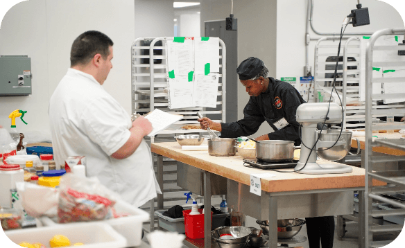 Student working in a culinary training kitchen, preparing food at a workstation.