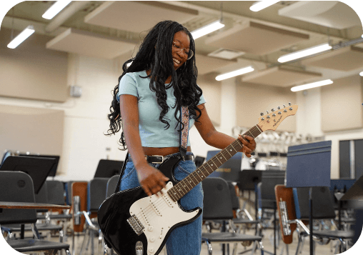 Student playing an electric guitar in a school music classroom.