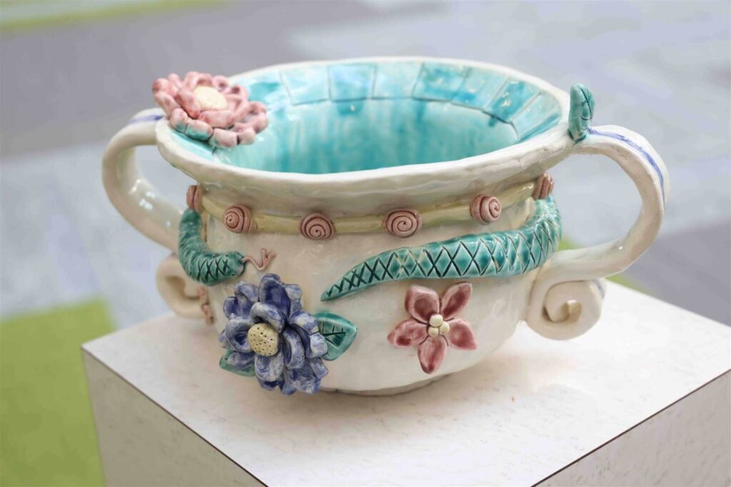 Decorative ceramic bowl displayed on a pedestal, featuring sculpted flowers and leaf designs.