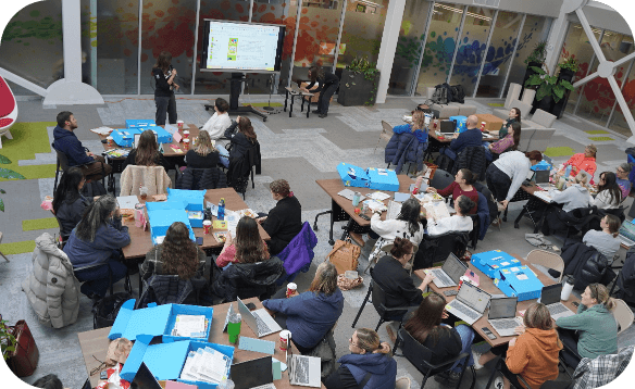 Participants seated at tables during a workshop or professional learning session in a large meeting space.